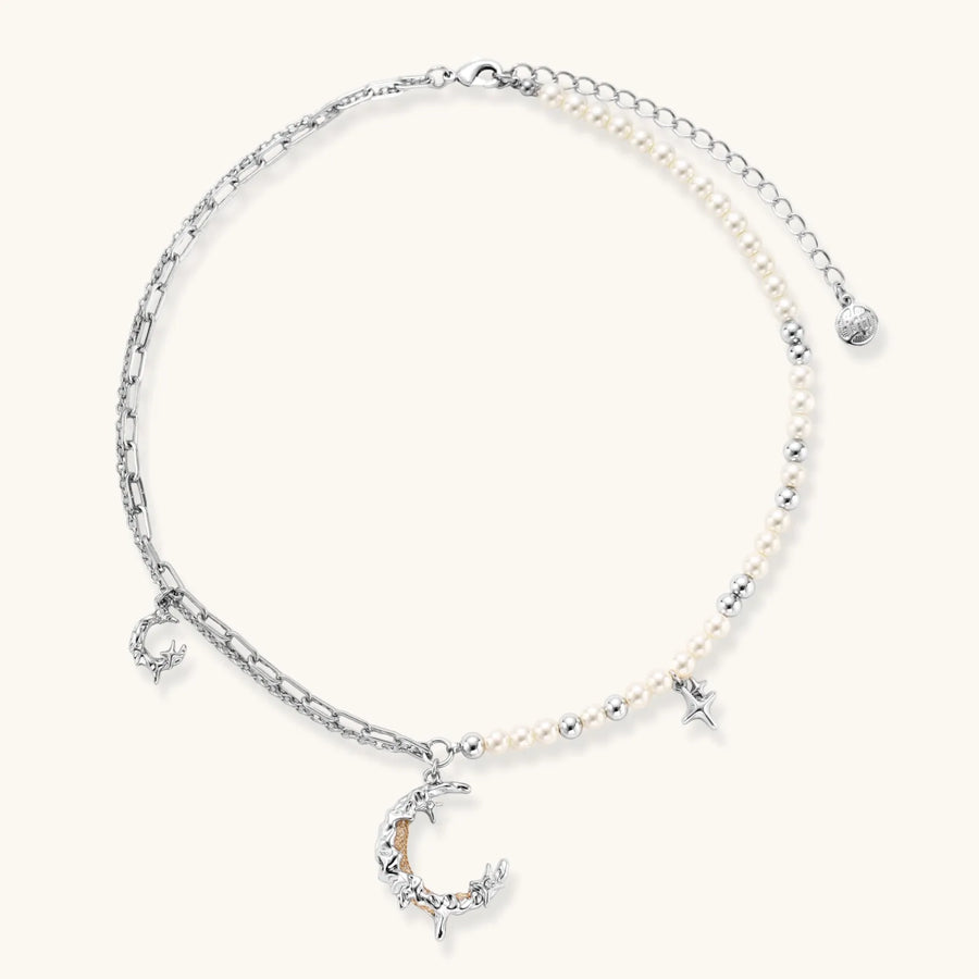 Silver-toned crescent moon pendant with star accents on pearl and chain necklace against white background.