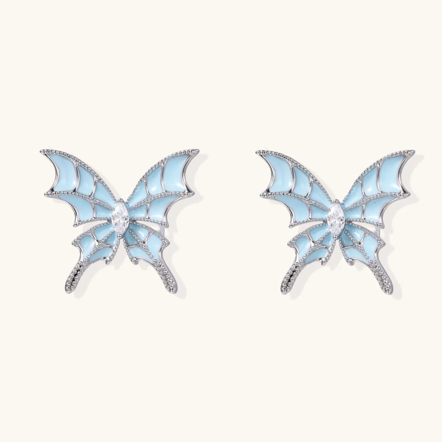 Long silver-tone earrings with powder blue enamel butterfly studs and flowing chain tassels on cream background