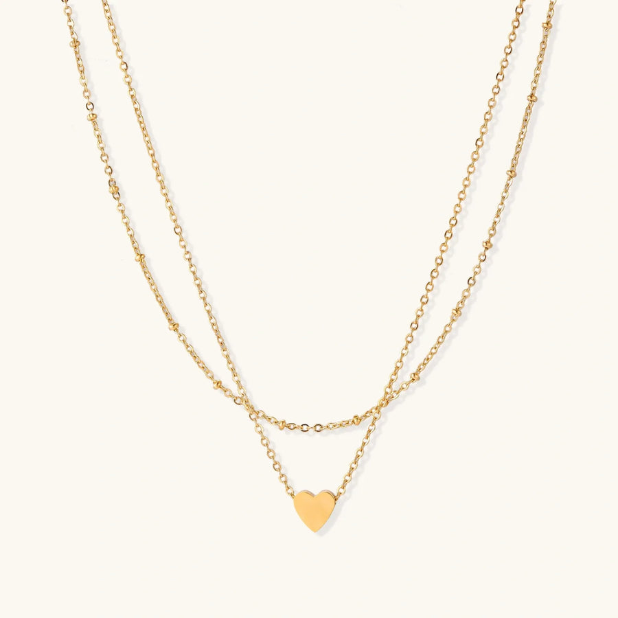 Delicate double-chain gold necklace with tiny heart pendant on cream background
