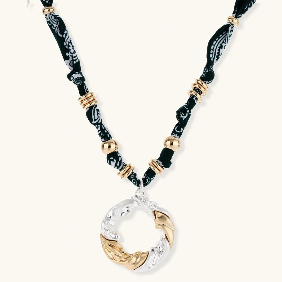 Adjustable necklace with black paisley fabric cord, gold metal spacers, and clear twisted pendant on cream background