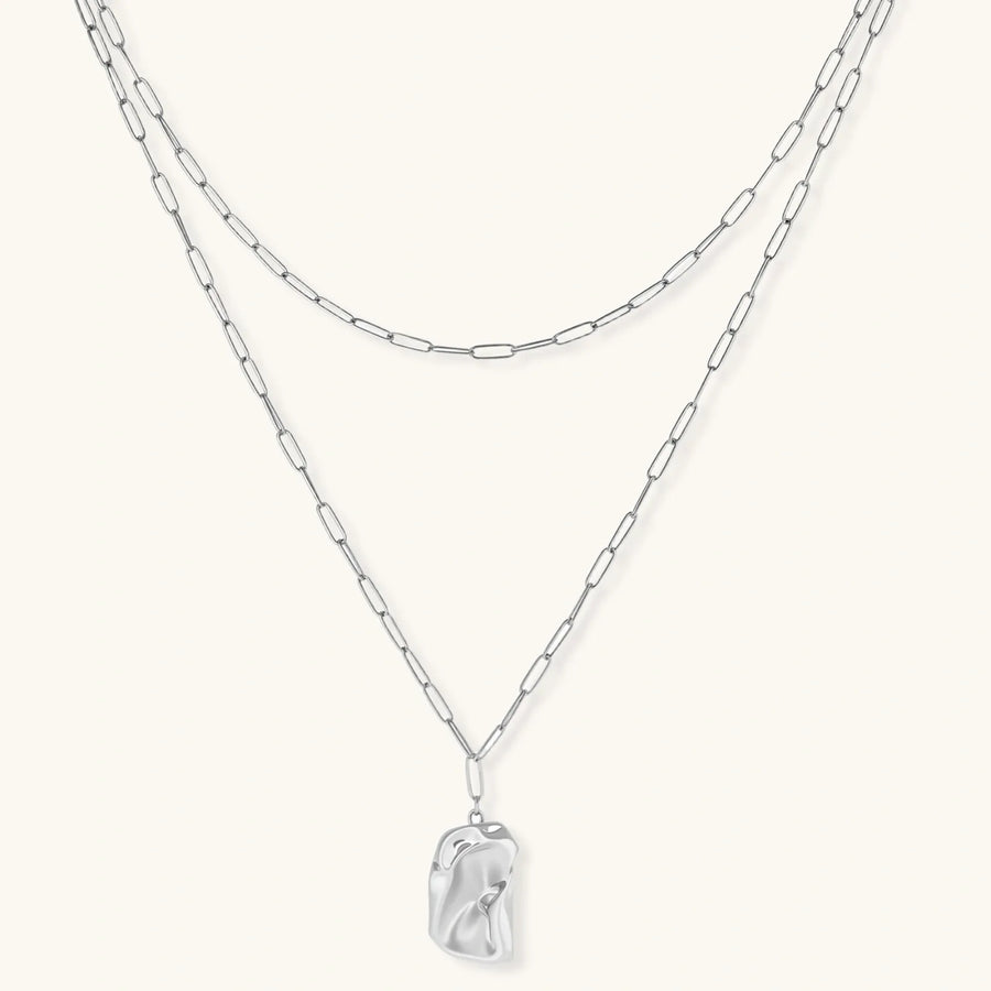 Silver layered necklace with organic flowing pendant in eco-zinc alloy on neutral background, showing adjustable chain design.