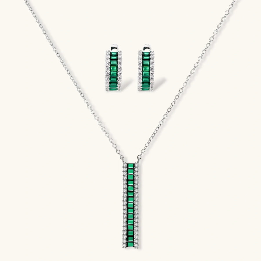 White gold plated jewelry set with emerald green rectangular stones and clear crystals in geometric rows on white background.