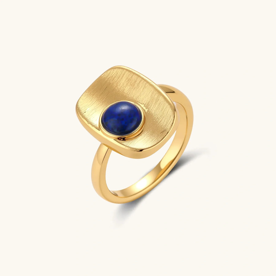 Adjustable gold-plated ring with textured square setting featuring a round blue lapis lazuli stone on cream background.