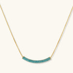 Gold-plated curved necklace and hoop earrings with turquoise cubic zirconia stones on white background.