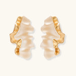 Sculptural wave-textured statement earrings with flowing organic ridges in metallic finish on cream background