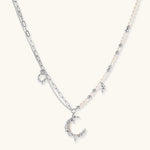Silver-toned crescent moon pendant with star accents on pearl and chain necklace against white background.