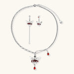 Silver-tone crown pendant with red zirconia stones and matching asymmetrical earrings on cream background