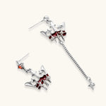 Silver-tone crown pendant with red zirconia stones and matching asymmetrical earrings on cream background