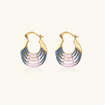 Gold hoop earrings with gradient blue-to-pink enamel in ribbed fan design on beige background