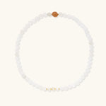 Three layered white beaded bracelets with carved orange agate lotus centerpiece and freshwater pearls on cream background.