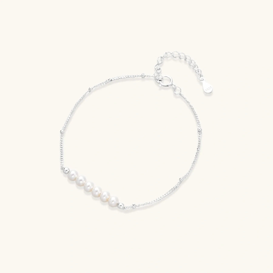 Delicate rhodium-plated silver chain bracelet with row of small baroque pearls centered on white background.