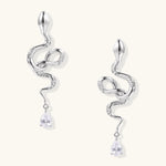 Silver snake-shaped drop earrings with crystal accents and teardrop stone dangles on cream background.