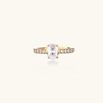 Gold-plated solitaire ring with oval zirconia center stone and pavé band on cream background