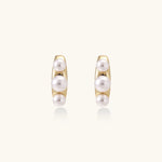 14K gold-plated curved stud earrings with three white freshwater pearls aligned vertically on cream background