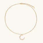 Gold crescent moon pendant with graduated white pearls on delicate chain against cream background
