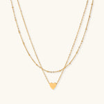 Delicate double-chain gold necklace with tiny heart pendant on cream background