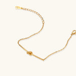 Delicate gold chain bracelet with minimalist bar and centered knot detail on cream background