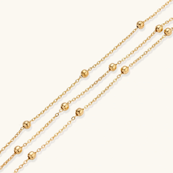 Three-strand gold-plated bracelet with clustered ball beads and adjustable clasp on cream background