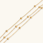 Three-strand gold-plated bracelet with clustered ball beads and adjustable clasp on cream background