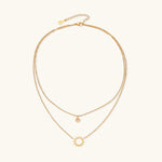 Gold layered necklace set with sunburst and smiley face pendants on delicate chains against white background.
