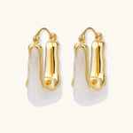 Sculptural gold-plated hoop earrings with flowing curved design and lever-back closure on cream background.