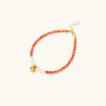 Beaded bracelet with coral-orange carnelian stones, white pearls, and gold heart charm on cream background
