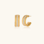 Textured gold huggie hoop earrings with raised ribbed rows creating dimensional sculptural design on cream background