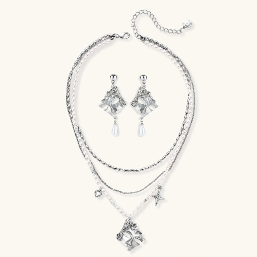 Ornate silver-toned masquerade mask jewelry set featuring rhinestone details and pearl drop earrings on white background.