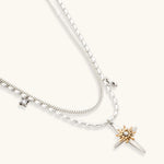 Layered silver-toned necklace set with cross pendant and gold sun charm detail, matching drop earrings on white background.