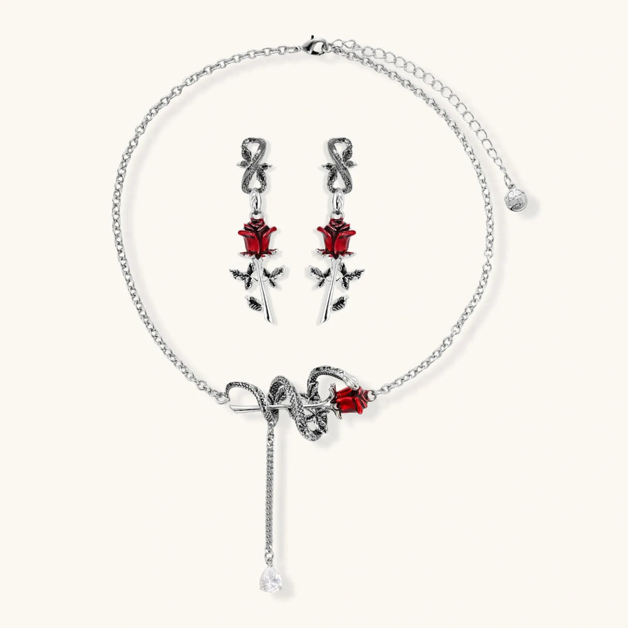 Gothic jewelry set with silver snake designs holding red enamel roses, featuring detailed leaf stems on cream background