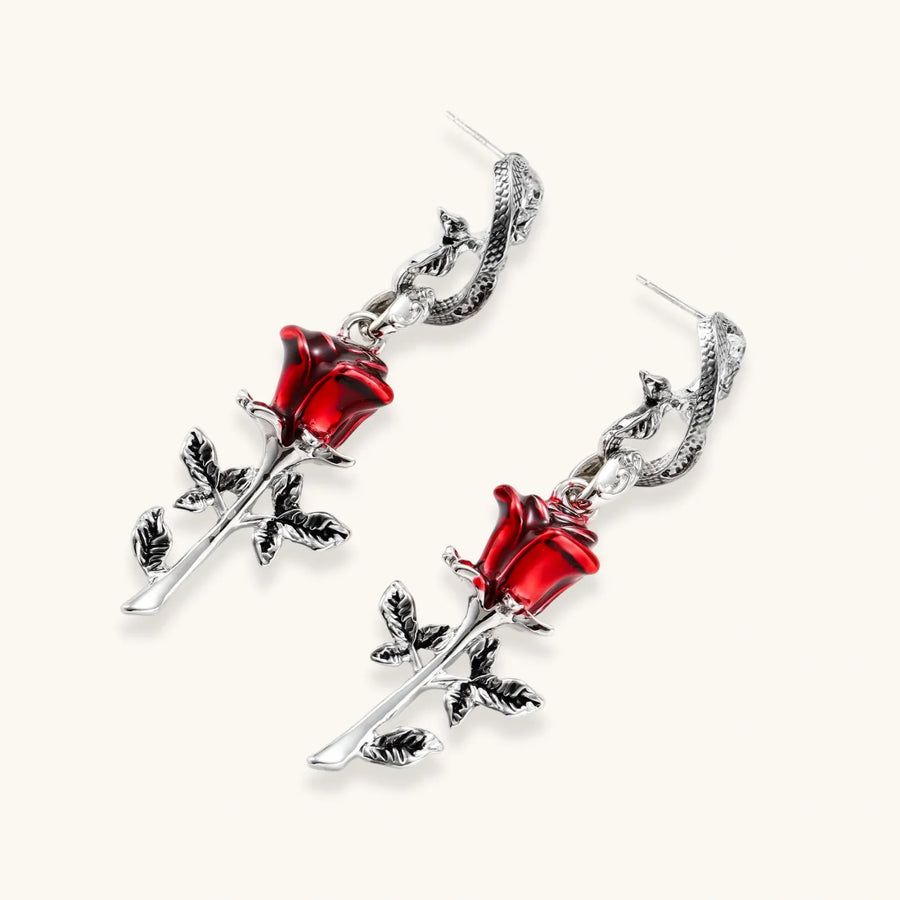 Gothic jewelry set with silver snake designs holding red enamel roses, featuring detailed leaf stems on cream background