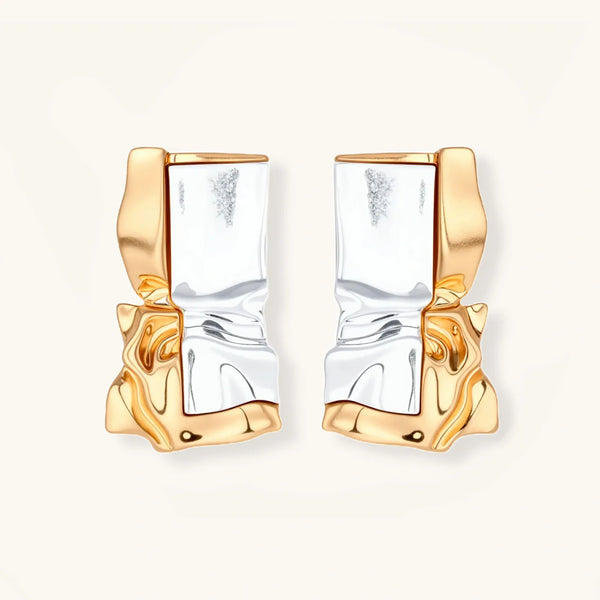 Close-up of avant-garde sculptural earrings with flowing liquid metal design in gold and silver tones on white background.