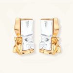 Close-up of avant-garde sculptural earrings with flowing liquid metal design in gold and silver tones on white background.