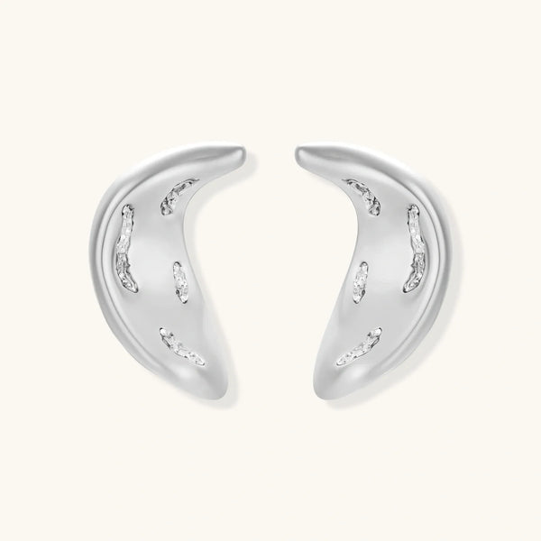 Curved crescent-shaped earrings in gold and silver with scattered perforated details on neutral background.