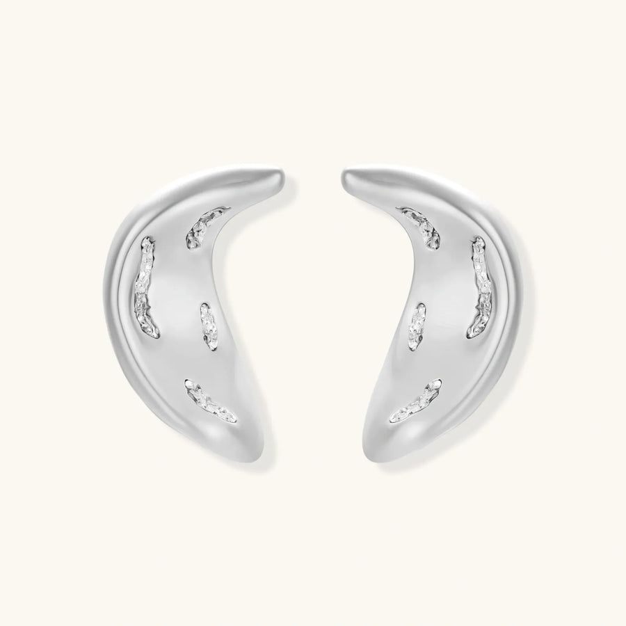 Curved crescent-shaped earrings in gold and silver with scattered perforated details on neutral background.