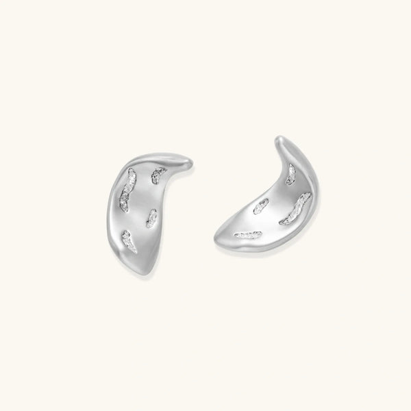 Curved crescent-shaped earrings in gold and silver with scattered perforated details on neutral background.