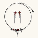 Gothic jewelry set with red resin cross pendants wrapped in dark metal chains on cream background.