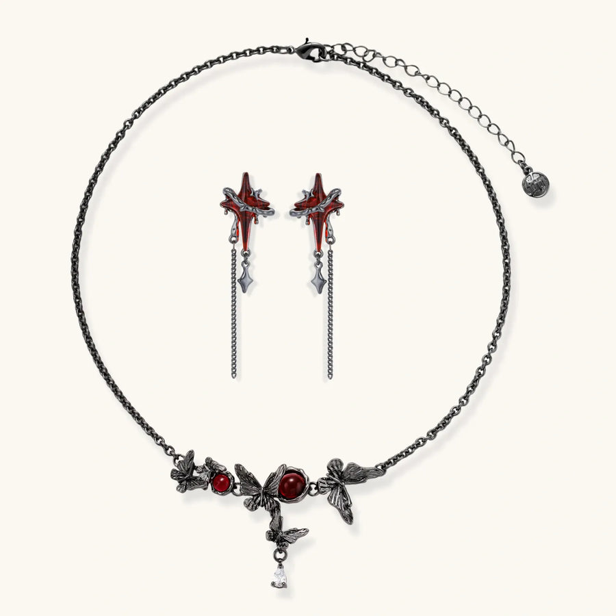 Gothic jewelry set with red resin cross pendants wrapped in dark metal chains on cream background.