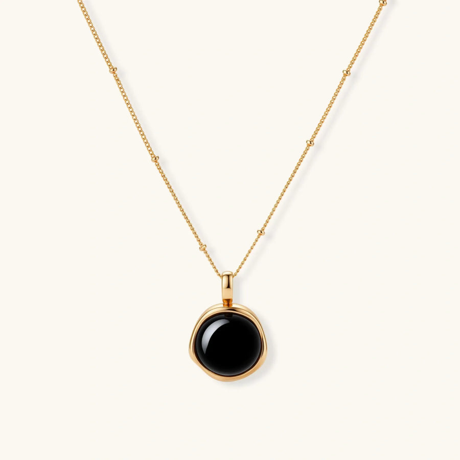 Circular black agate pendant on gold-plated sterling silver chain against cream background, showing modern minimalist design.