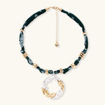 Adjustable necklace with black paisley fabric cord, gold metal spacers, and clear twisted pendant on cream background