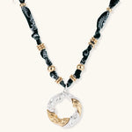 Adjustable necklace with black paisley fabric cord, gold metal spacers, and clear twisted pendant on cream background