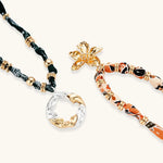 Adjustable necklace with black paisley fabric cord, gold metal spacers, and clear twisted pendant on cream background
