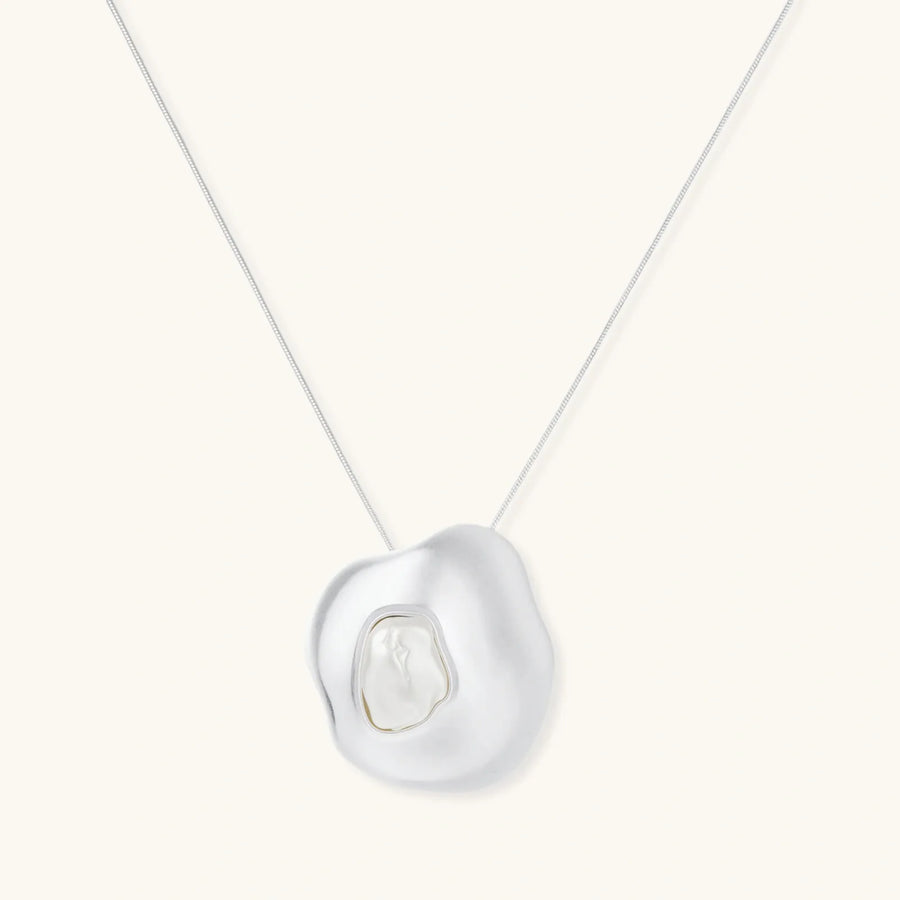 Sculptural silver necklace with flowing organic pendant featuring centered baroque pearl on white background.