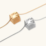Close-up of a silver-toned molten cube pendant necklace with organic flowing texture on a minimalist chain