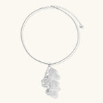 Modern sculptural pendant necklace with twisted metallic design on delicate silver chain against neutral background.