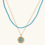 Gold-plated turquoise jewelry set with circular medallion pendant, beaded necklace, and matching stud earrings on white background