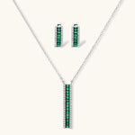 White gold plated jewelry set with emerald green rectangular stones and clear crystals in geometric rows on white background.