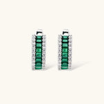 White gold plated jewelry set with emerald green rectangular stones and clear crystals in geometric rows on white background.