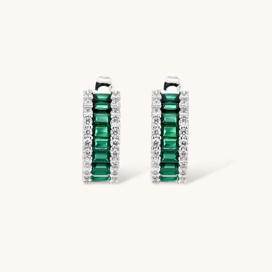 White gold plated jewelry set with emerald green rectangular stones and clear crystals in geometric rows on white background.
