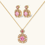 Ornate gold-plated jewelry set with rose pink zirconia center stones and crystal accents on cream background.